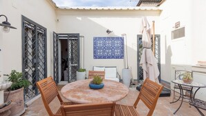 Eine Terrasse mit einem runden Tisch, vier Holzstühlen, Kübelpflanzen und einer blau gemusterten Wandfliese.