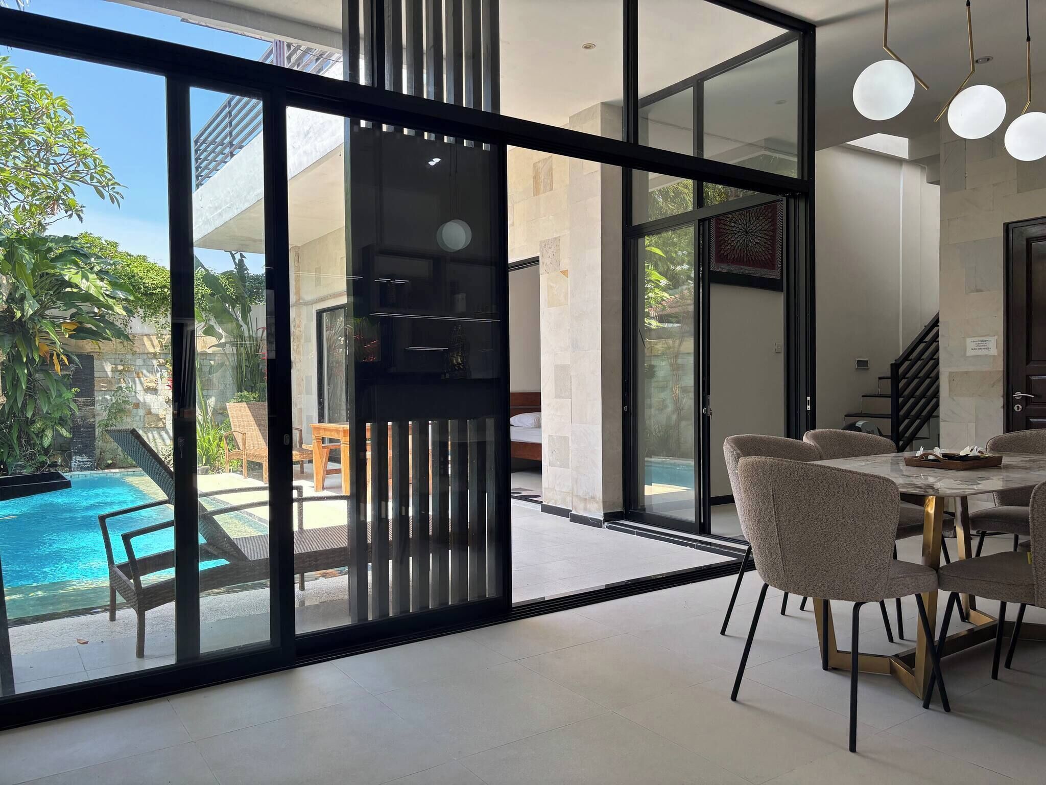 A modern interior with a glass wall leading to a pool area, a dining area with chairs, and a staircase.