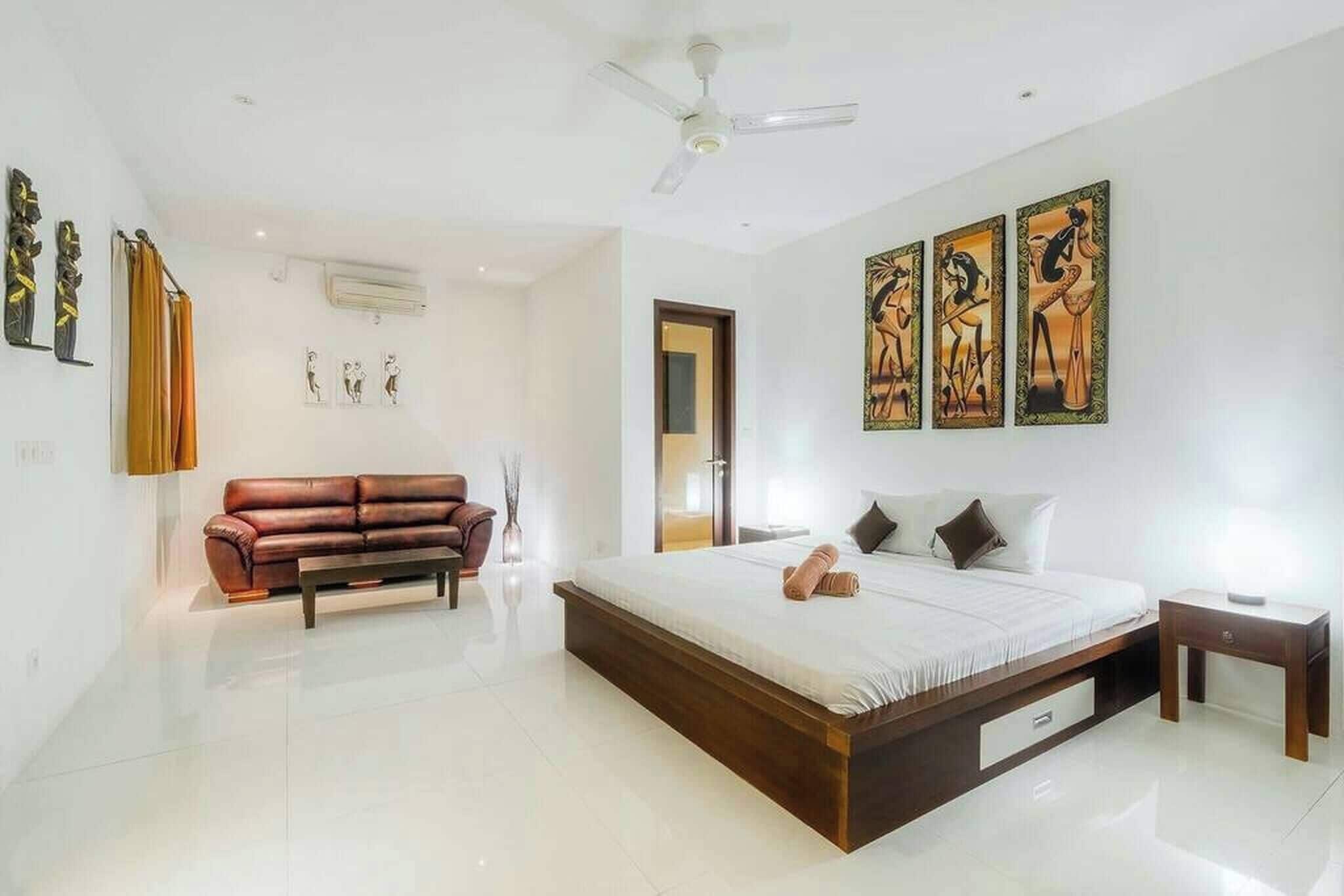 A modern bedroom with a large bed, a brown leather sofa, and three framed artworks on the wall.