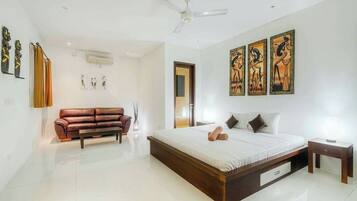 A modern bedroom with a large bed, a brown leather sofa, and three framed artworks on the wall.