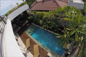A rooftop pool with wooden deck chairs, surrounded by lush greenery and a stone wall. - 3 BR, 250 Sqmt Villa, Terrace, 10 min Finns (Canggu)