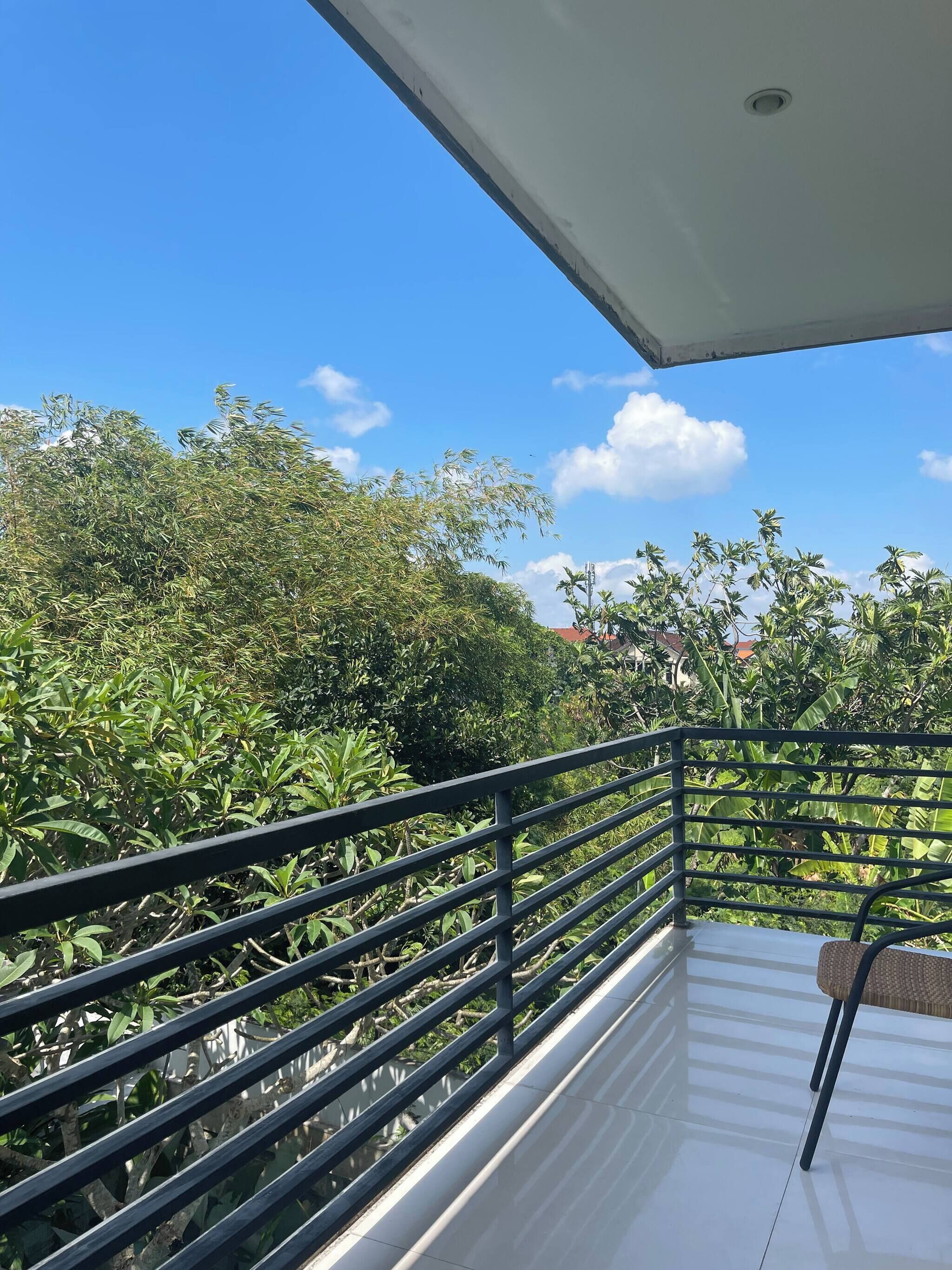 A balcony with a metal railing overlooking a lush garden with various plants and trees.