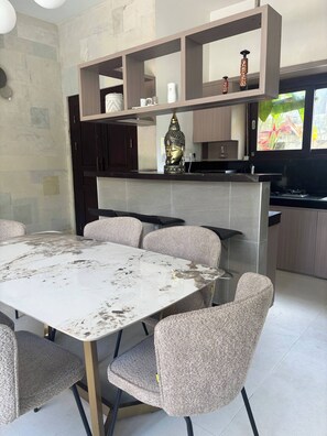 A modern kitchen with a marble countertop, a built-in oven, and a dining area with a large table and six chairs. - 3 BR, 250 Sqmt Villa, Terrace, 10 min Finns (Canggu)