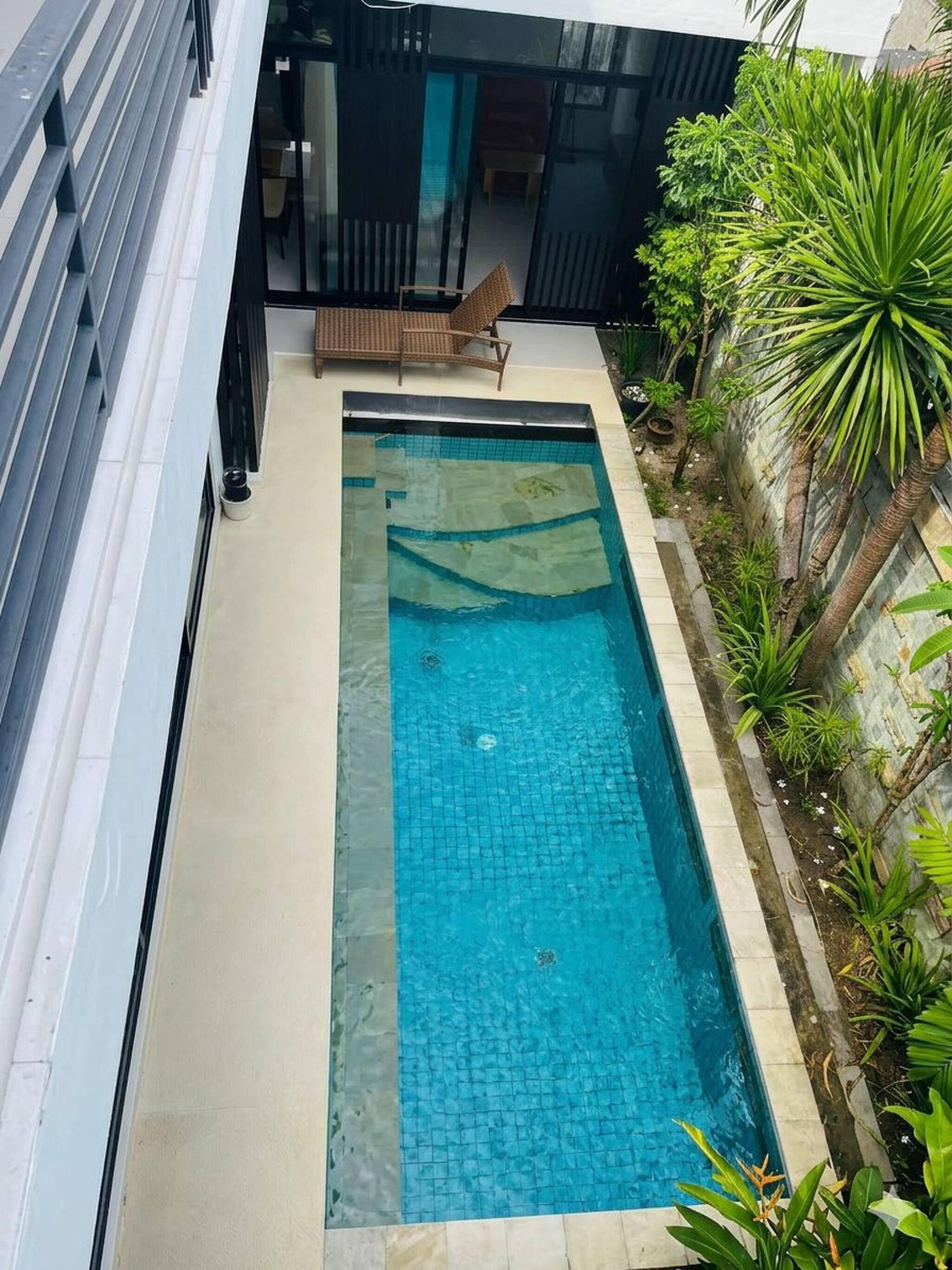 A rectangular swimming pool with a tiled deck, surrounded by a low wall and various plants.
