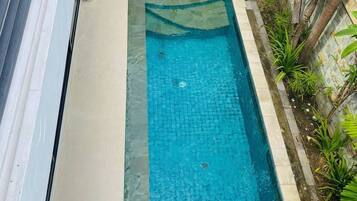 A rectangular swimming pool with a tiled deck, surrounded by a low wall and various plants.