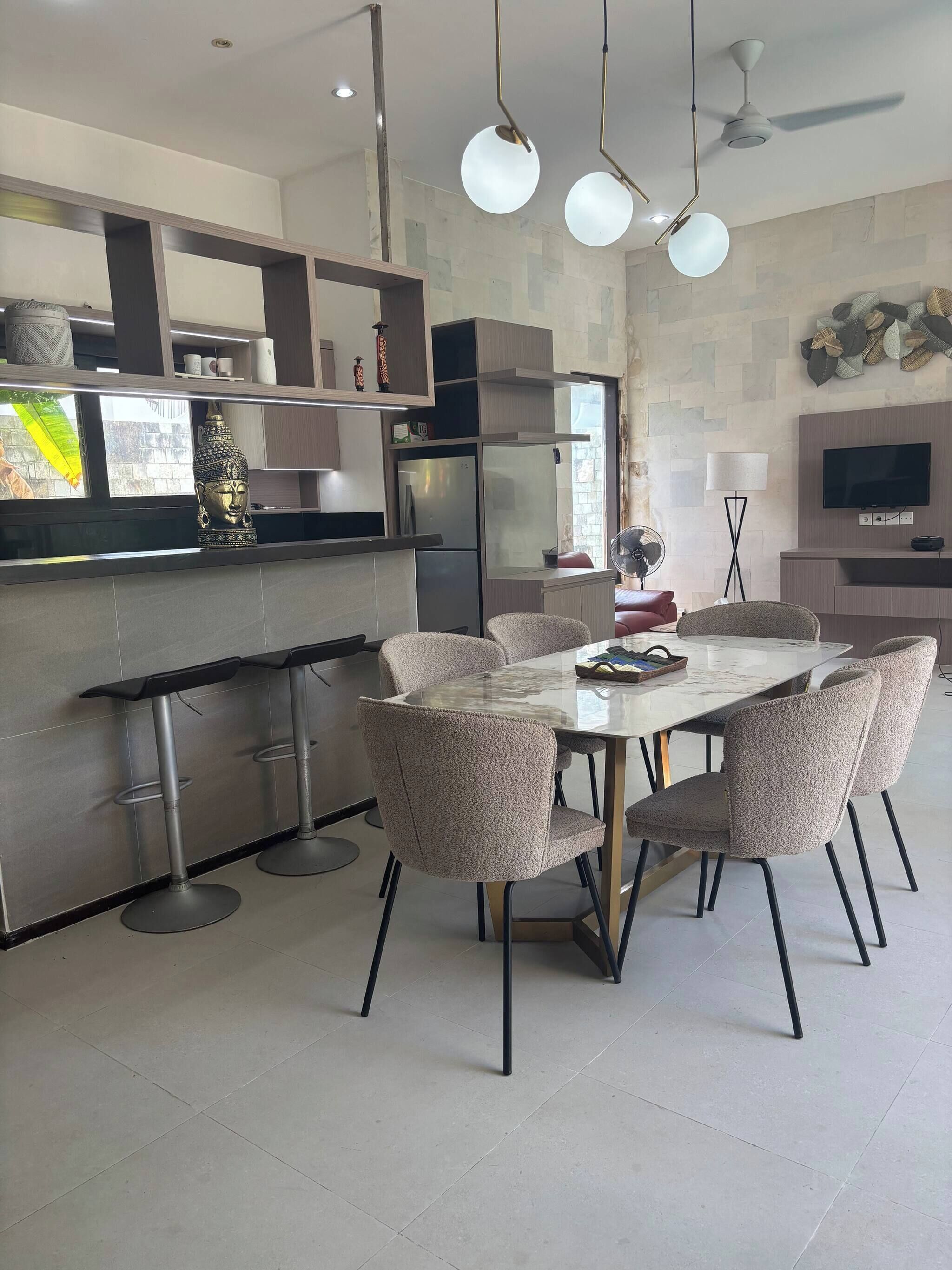 A modern kitchen with a built-in refrigerator, a dining area with a marble table and upholstered chairs, and a flat-screen TV mounted on the wall.