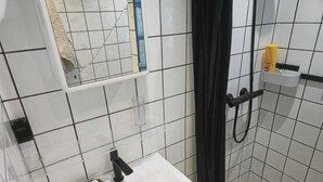 Kylpyhuone, jossa on valkoinen pesuallas, peili, suihkuverho ja hylly, jossa on hygieniatuotteita.
