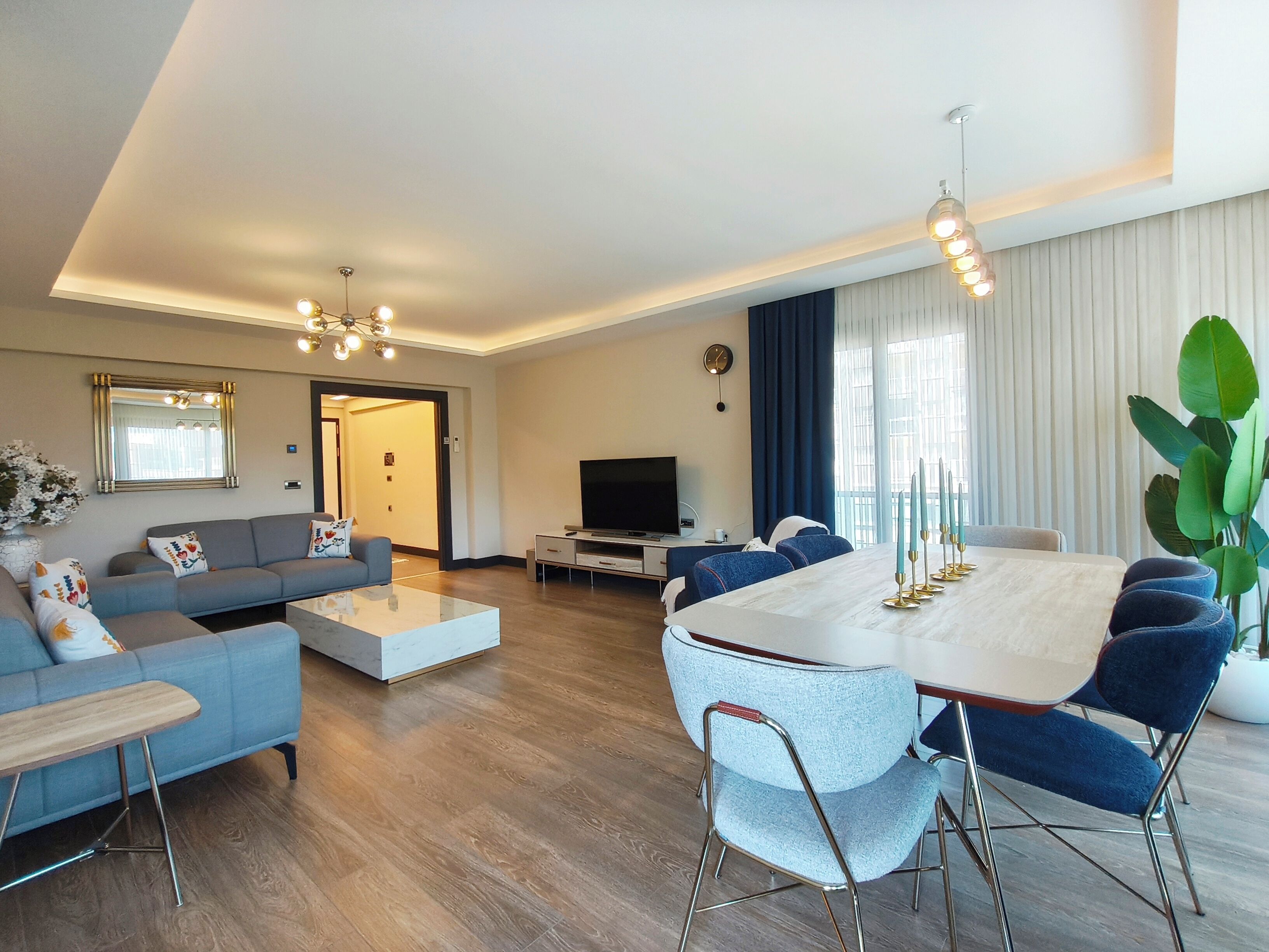 A modern living room with a sofa, coffee table, TV, and dining area with chairs and a table.