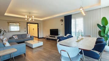 A modern living room with a sofa, coffee table, TV, and dining area with chairs and a table.