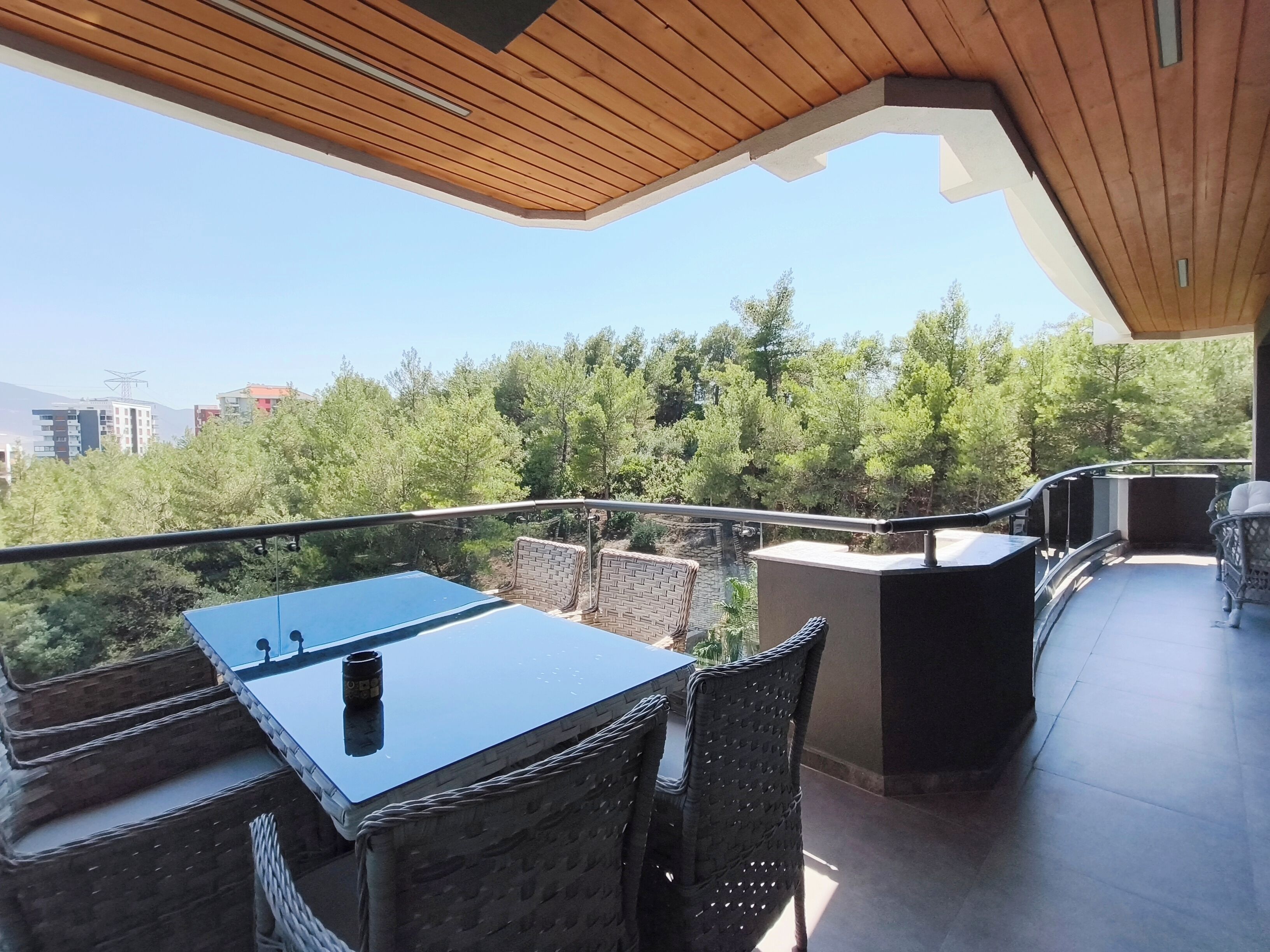 An outdoor patio with a table and chairs, a grill, and a view of trees and buildings.