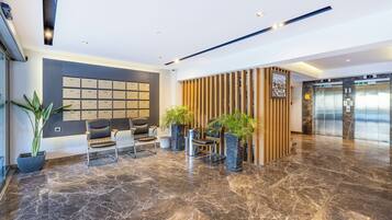 A modern lobby with a marble floor, seating area, reception desk, and an elevator.