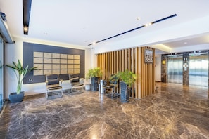 Un hall d’entrée moderne avec un sol en marbre, un espace salon, un comptoir de réception et un ascenseur.