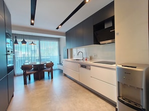 A modern kitchen with a dining area, featuring a built-in oven, a dishwasher, and a water dispenser.