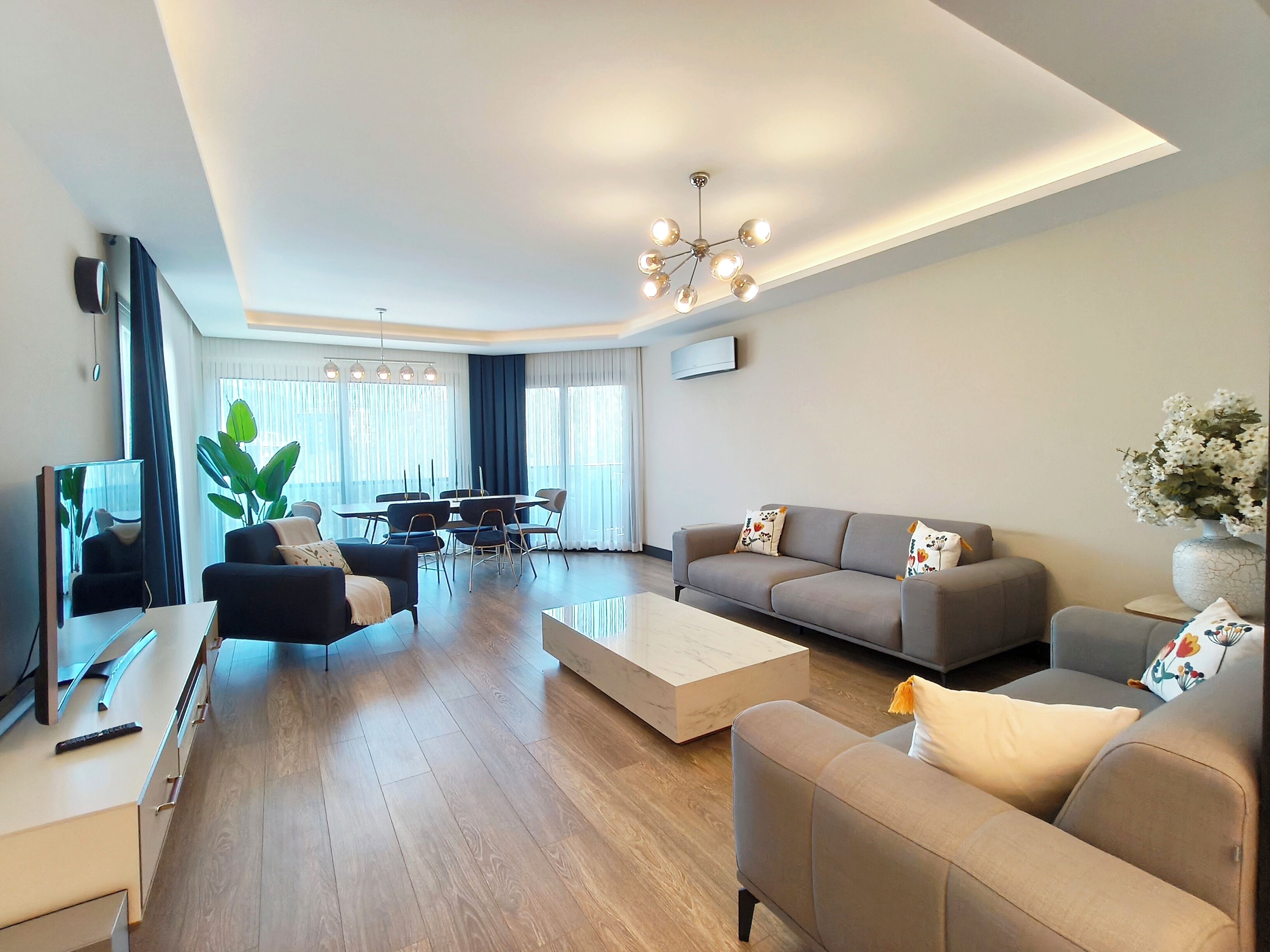 A modern living room with a sofa, coffee table, and a dining area with chairs and a table.