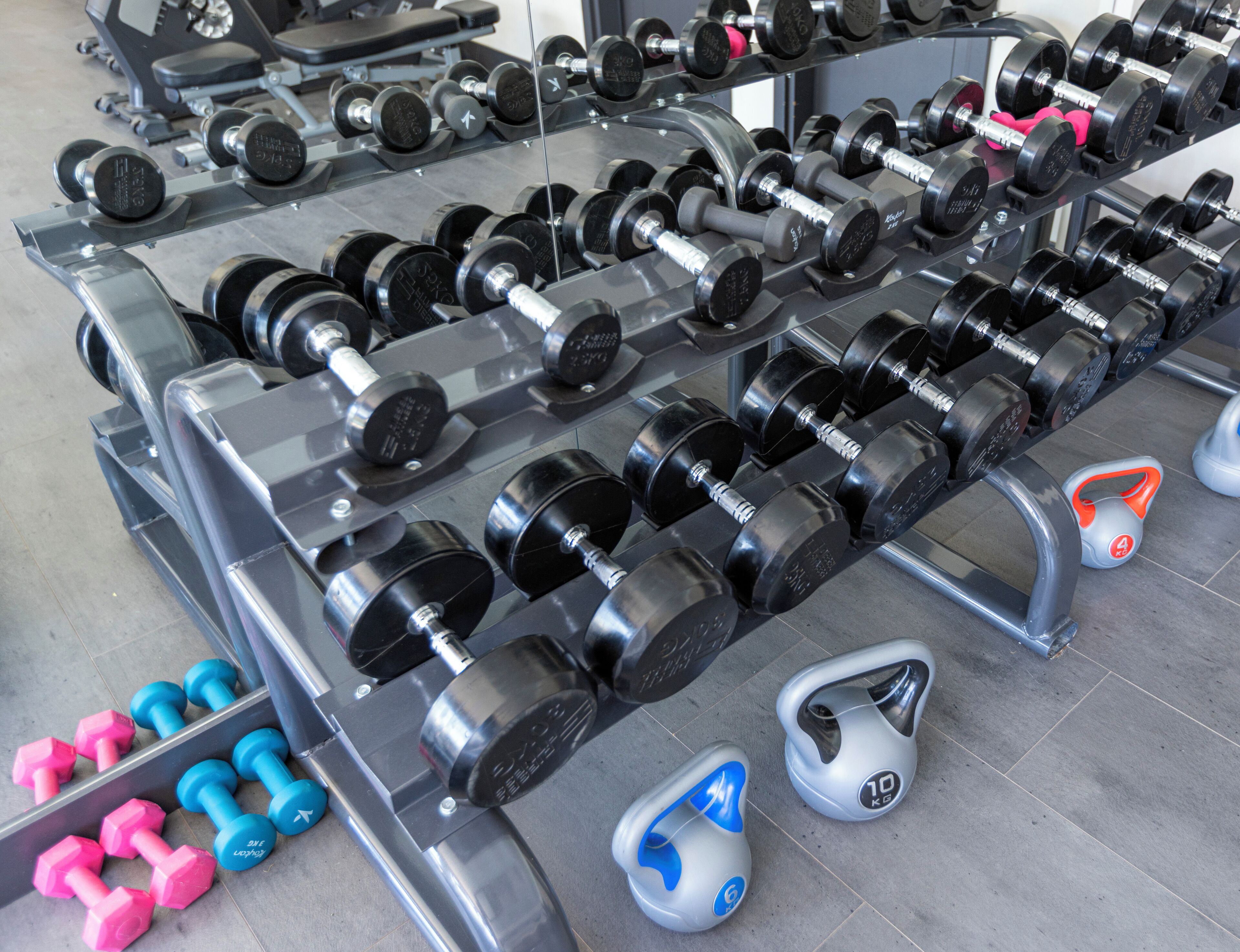 A gym with various weightlifting equipment, including dumbbells and kettlebells, arranged on racks.