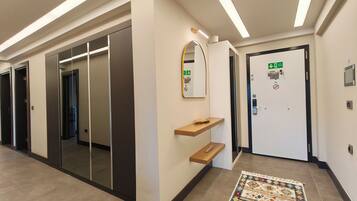 A hallway with a mirrored wall, a door with an emergency exit sign, and a patterned rug on the floor.