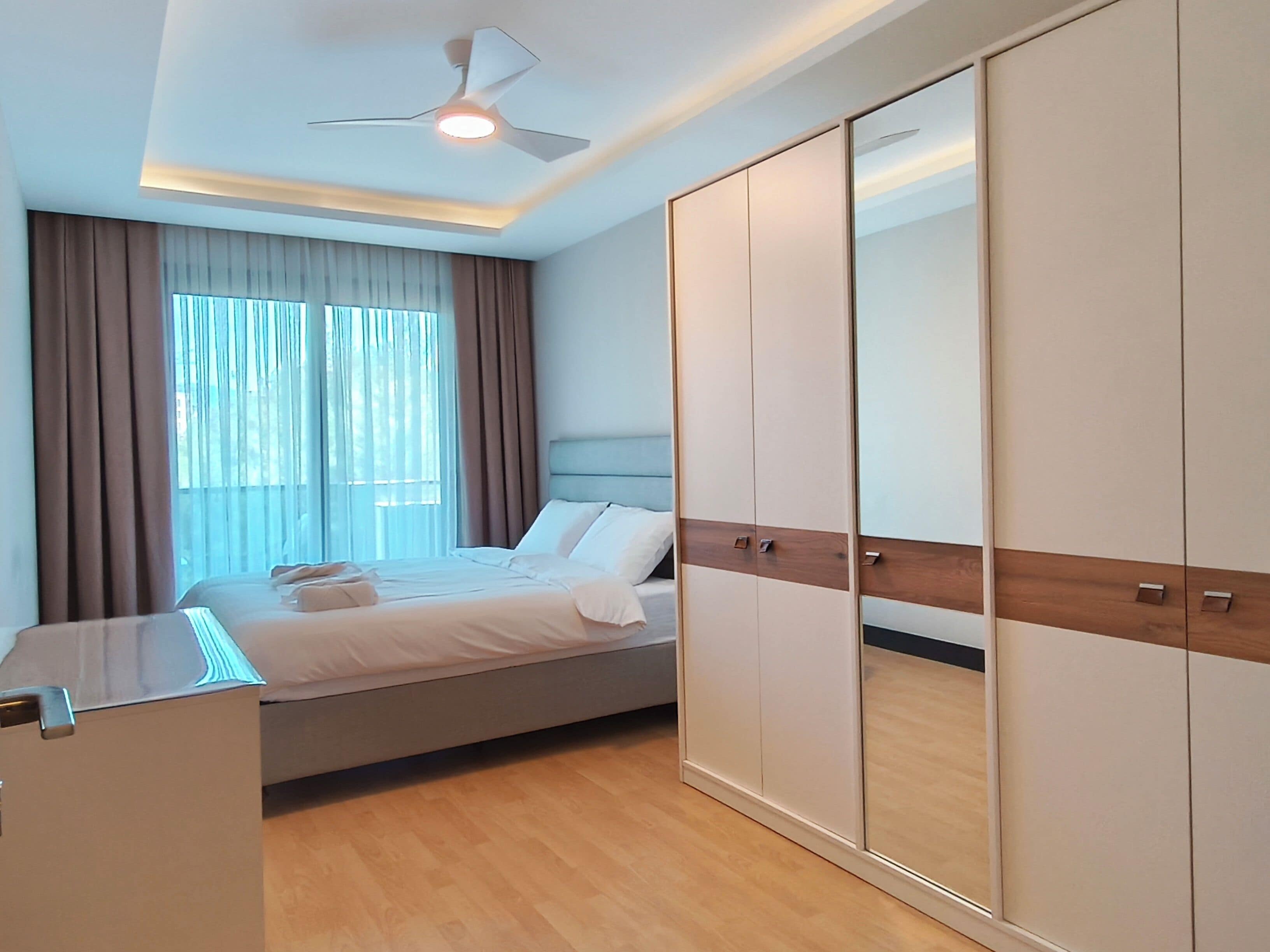 A modern bedroom with a bed, a wardrobe, and a ceiling fan.