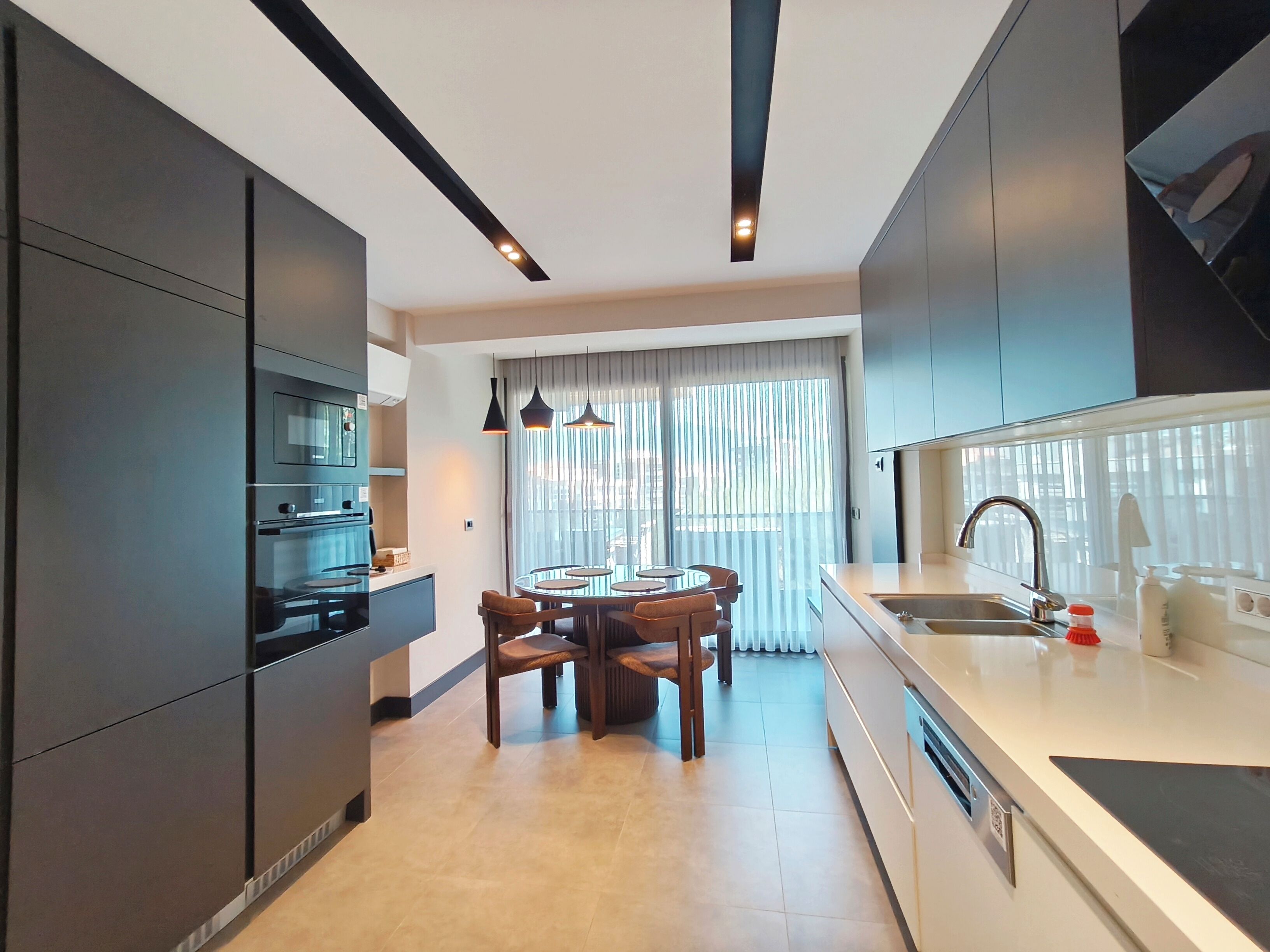 A modern kitchen with a dining area, featuring dark cabinetry, a central island, and pendant lighting.