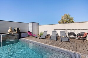 A rooftop pool area with a Buddha statue, lounge chairs, and a clear blue sky.