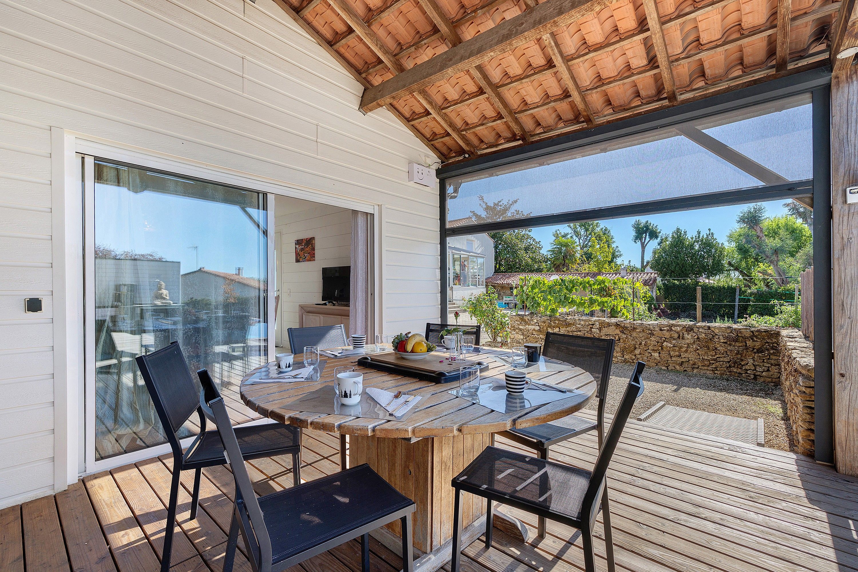 Un espace extérieur abrité, aménagé pour les repas, avec une table pour deux, entourée de chaises, et une vue sur le jardin grâce à de grandes fenêtres.