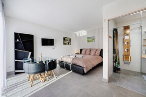 A modern bedroom with a bed, a desk, and a shower area.