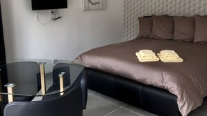 Una camera d'albergo moderna con un letto, una TV a schermo piatto, un tavolino in vetro e un'opera d'arte appesa al muro.