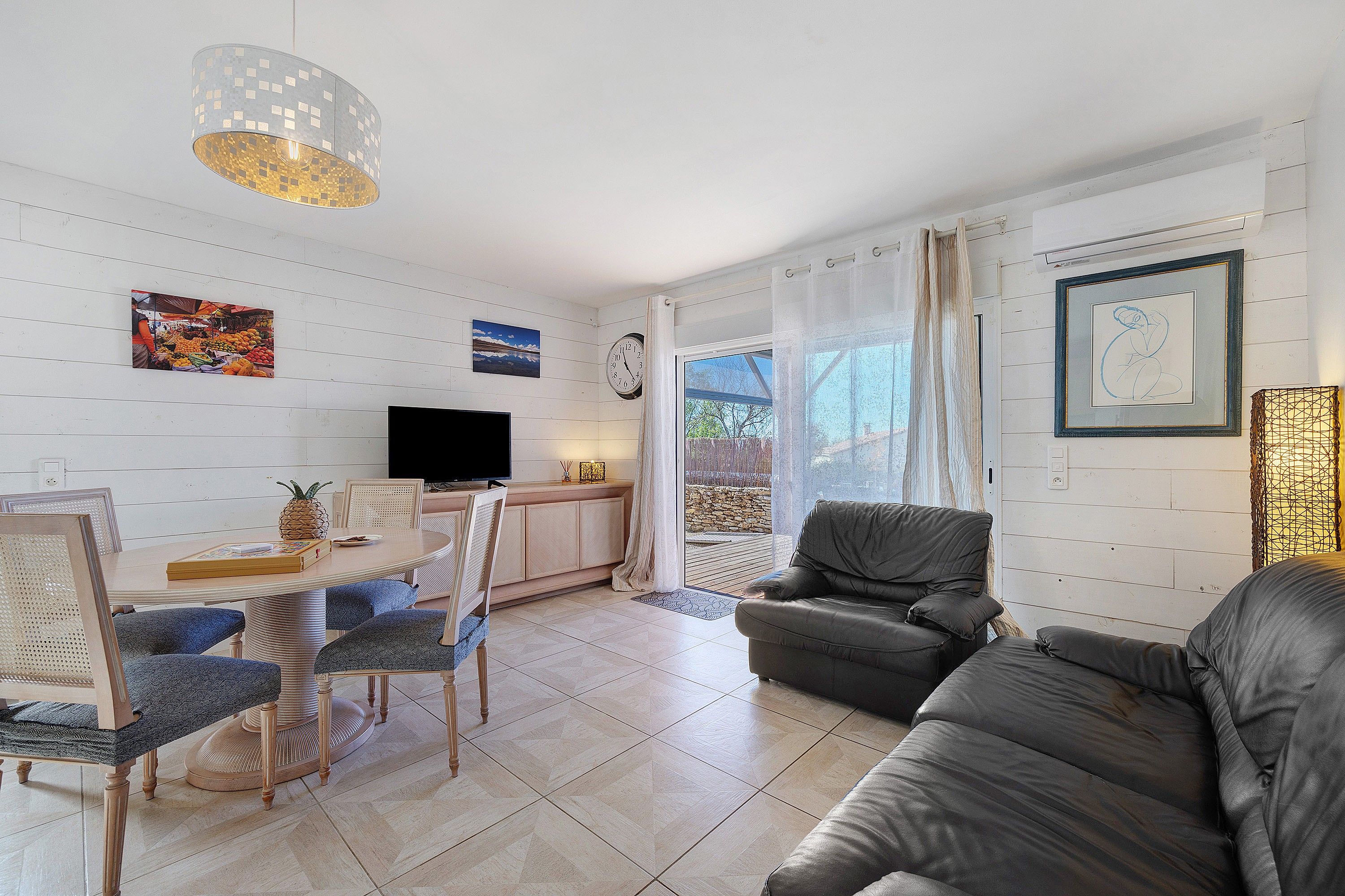 A modern living room with a dining area, a television, and artwork on the walls.