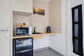 Eine kleine Küchenzeile mit Mikrowelle, Kaffeemaschine und kleinem Kühlschrank.