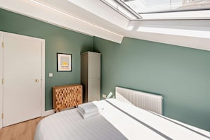 Ein Schlafzimmer mit Bett, Schrank, Heizkörper und einem Oberlicht.