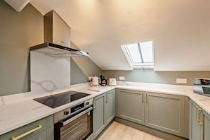 Eine kompakte Küche mit integriertem Herd, Backofen und Mikrowelle. Ein Fenster sorgt für natürliches Licht und es gibt eine kleine Arbeitsfläche mit Kaffeemaschine und Toaster.