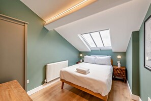 A bedroom with a sloped ceiling, a skylight, a bed with white bedding, a bedside table with a lamp, and a radiator. - Host & Stay | The Georgian Quarter @ Catharine V (Liverpool)