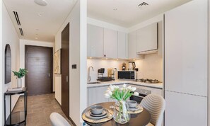 A modern kitchen with white cabinets, a microwave, and a coffee maker. There is a dining table with a vase of flowers and a chair.
