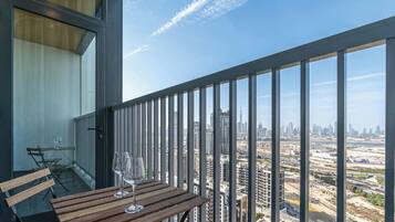 A balcony with a wooden table and two wine glasses, overlooking a cityscape with high-rise buildings.