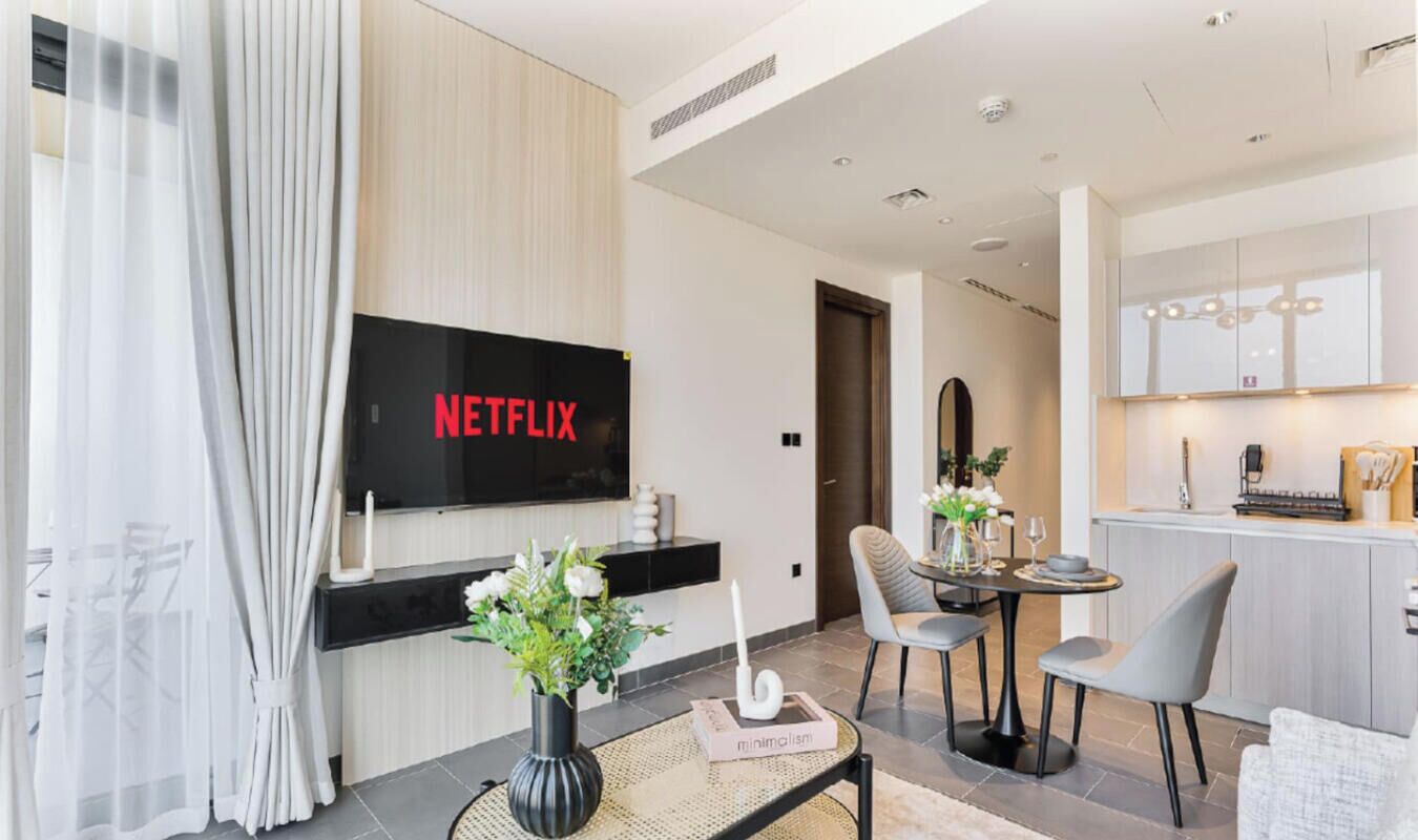 Een moderne woonkamer met een flatscreen televisie, een eethoek met een tafel en stoelen, en een keuken met een aanrecht en kasten.
