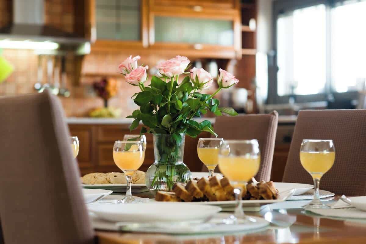 A dining table with a vase of flowers, plates of food, and glasses of a yellow beverage.