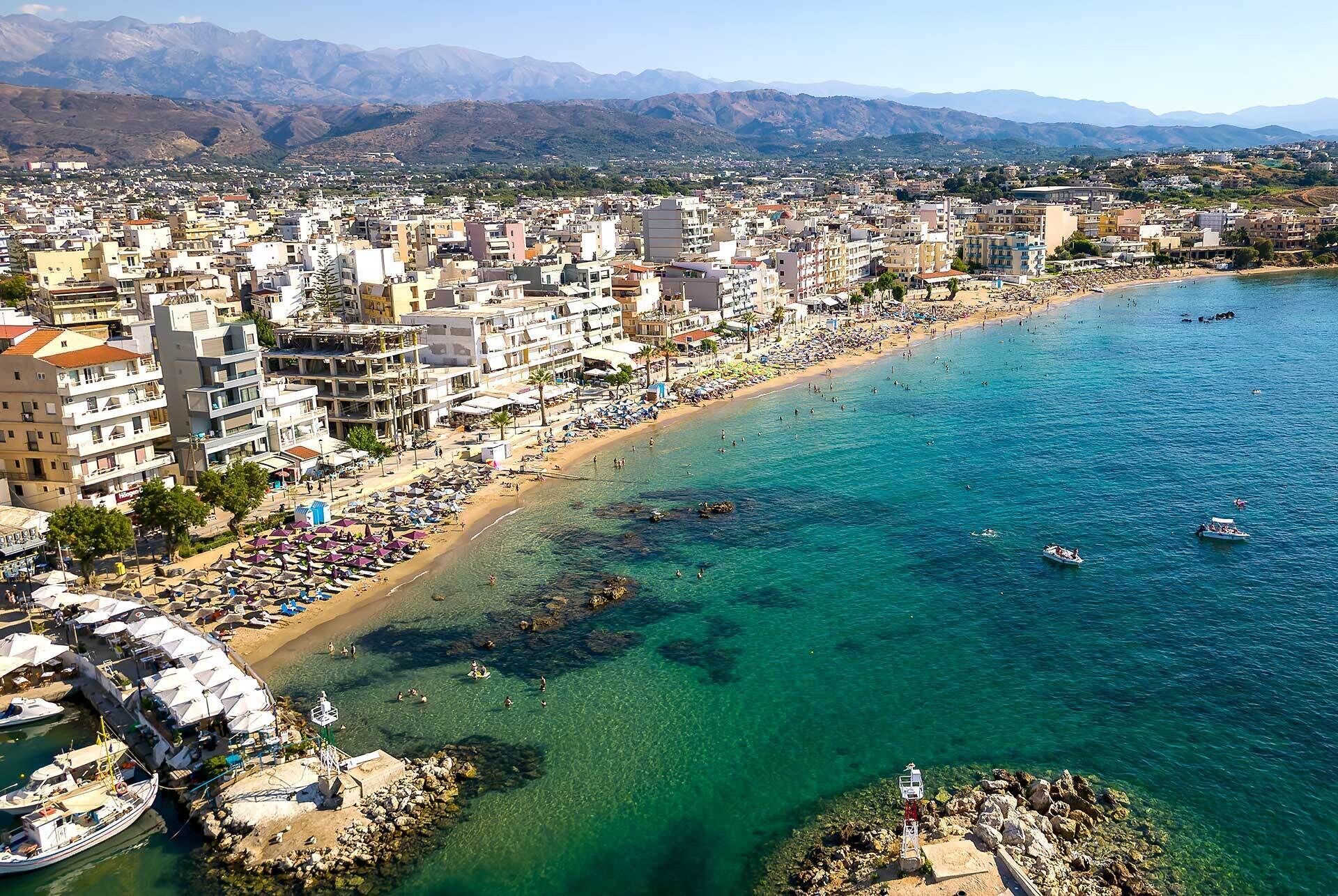 Un paysage urbain côtier avec une plage, des bâtiments et des montagnes en arrière-plan.