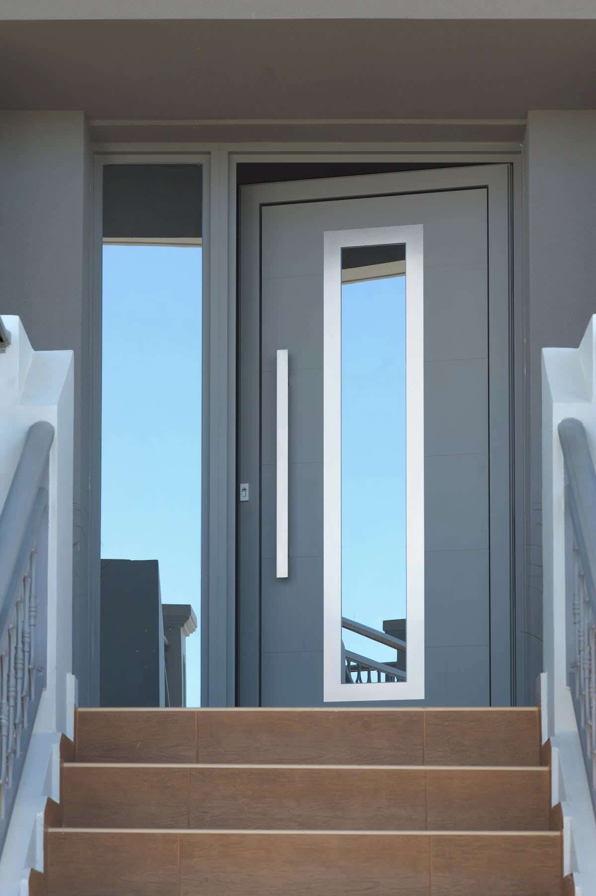 A modern entrance with a double door, a handrail on the stairs, and a clear view of the sky.
