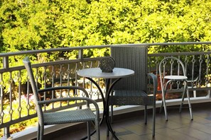 Ein Balkon mit Korbstühlen und einem kleinen runden Tisch, mit Blick auf einen gepflegten Heckenstreifen.