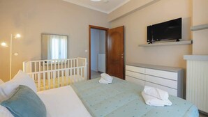 A hotel room with a bed, a crib, a television on a shelf, and a door leading to another room. - Solena - Garden Escape with Views near Chania (Tsikalaria)