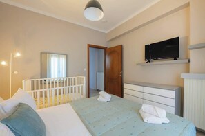 Ein Hotelzimmer mit einem Bett, einem Reisebettchen, einem Fernseher auf einem Regal und einer Tür zu einem anderen Raum.