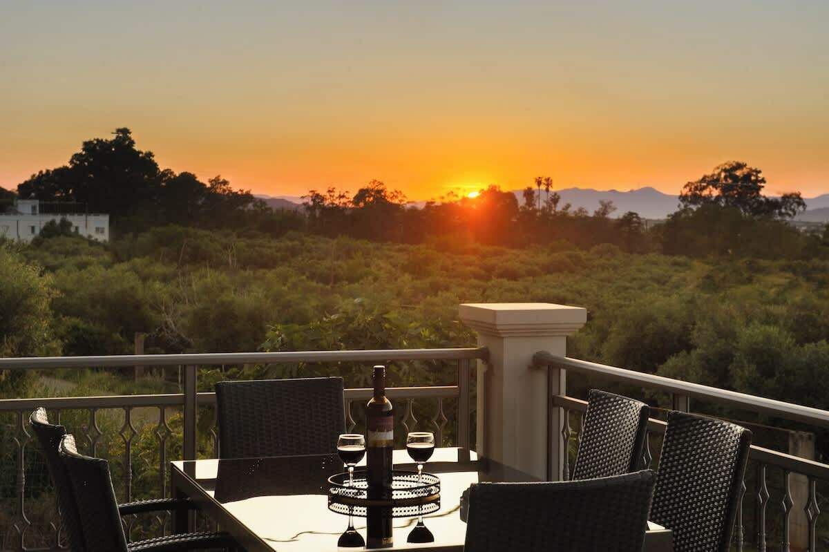 Une table avec des chaises et une bouteille, le tout placé devant un paysage au coucher du soleil.
