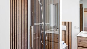 Un baño moderno con cabina de ducha de vidrio, paneles de madera, un lavamanos blanco y un mueble de madera.