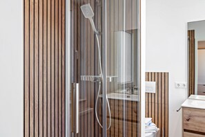 A modern bathroom with a glass shower enclosure, wooden paneling, a white sink, and a wooden cabinet. - Studio Apartment 'Möbliertes Radebeul' with Balcony and Wi-Fi (Radebeul)