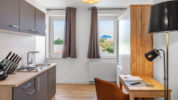 Cocina compacta con lavaplatos, armarios y comedor con una silla y mesa.