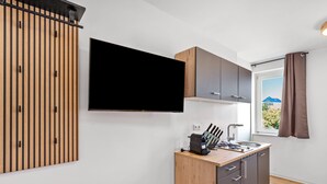 Una cocina moderna con televisor de pantalla plana montado en la pared, armarios de madera, una encimera con una cafetera y un ventanal con vistas al exterior.