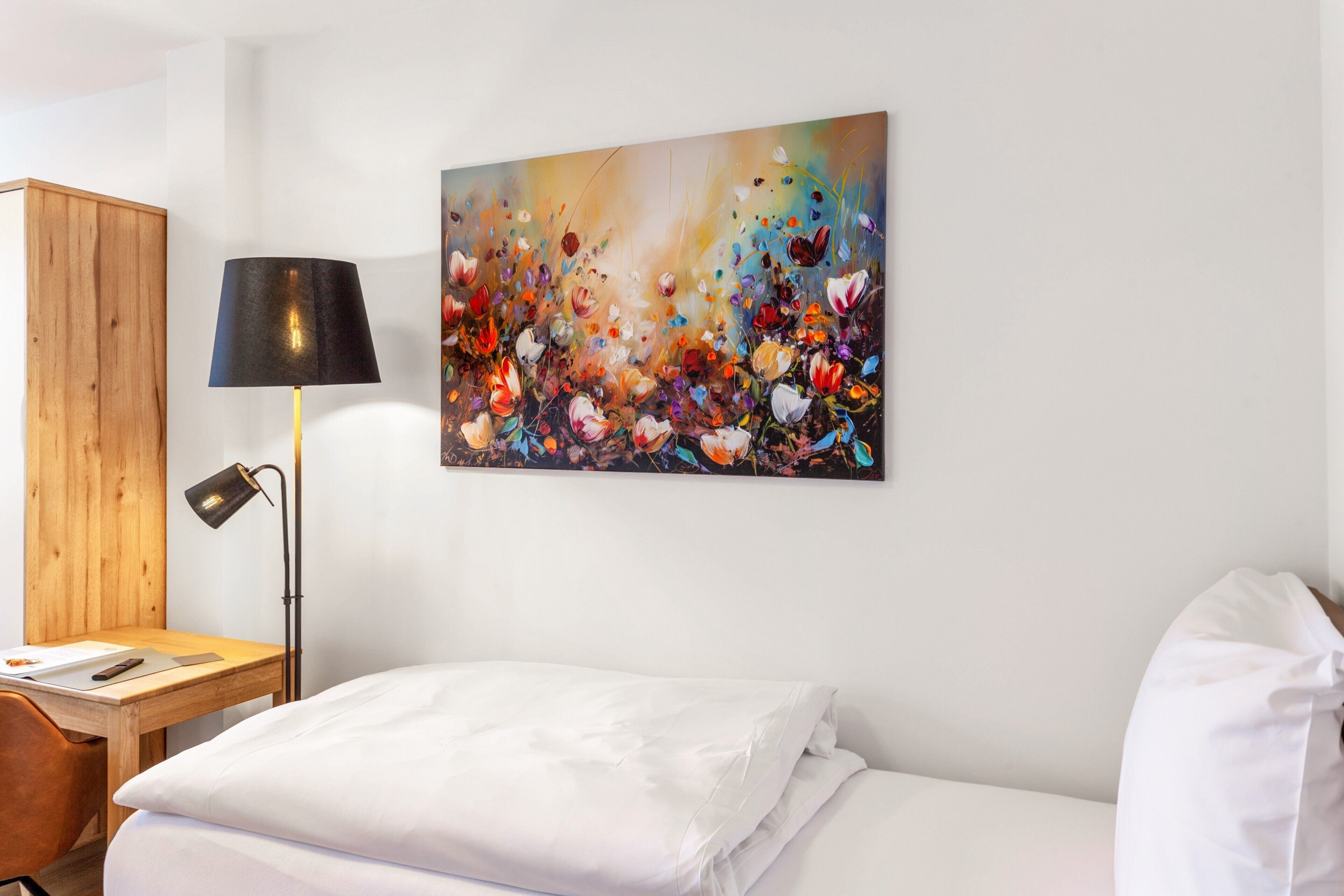 Una habitación de hotel con cama, escritorio con lámpara y un cuadro abstracto colorido en la pared.