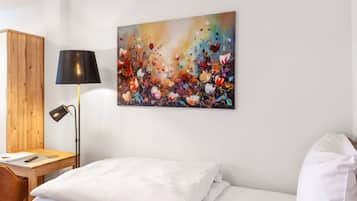 Ein Hotelzimmer mit einem Bett, einem Schreibtisch mit Lampe und einem farbenfrohen, abstrakten Gemälde an der Wand.