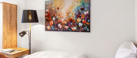 Una habitación de hotel con cama, escritorio con lámpara y un cuadro abstracto colorido en la pared.