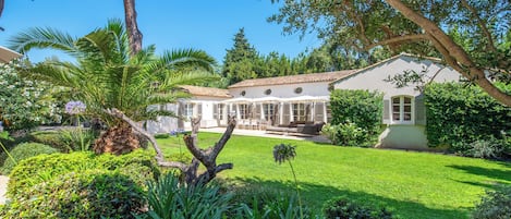 A house with a garden, a patio with outdoor furniture, and a large tree.