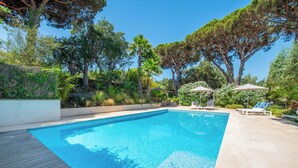 Une piscine rectangulaire avec une terrasse en bois d’un côté, entourée d’une végétation luxuriante et d’arbres.